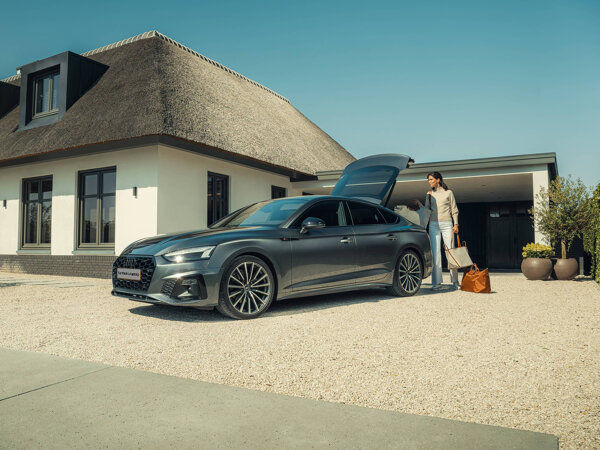 Vrouw met reistassen bij een grijze Audi met open achterklep